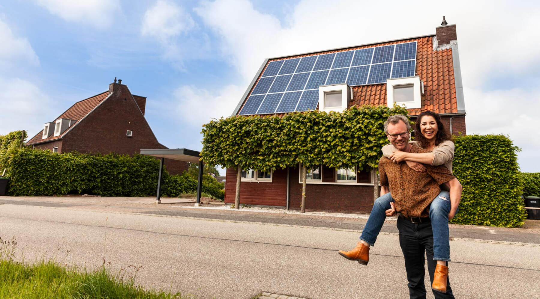 Een man en vrouw staan voor een huis met zonnepanelen op het dak.