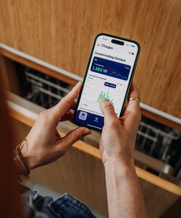Hand houdt telefoon vast met de Chargee app geopend. Staat bij vaatwasser en kijkt naar verwachte zonopwek.